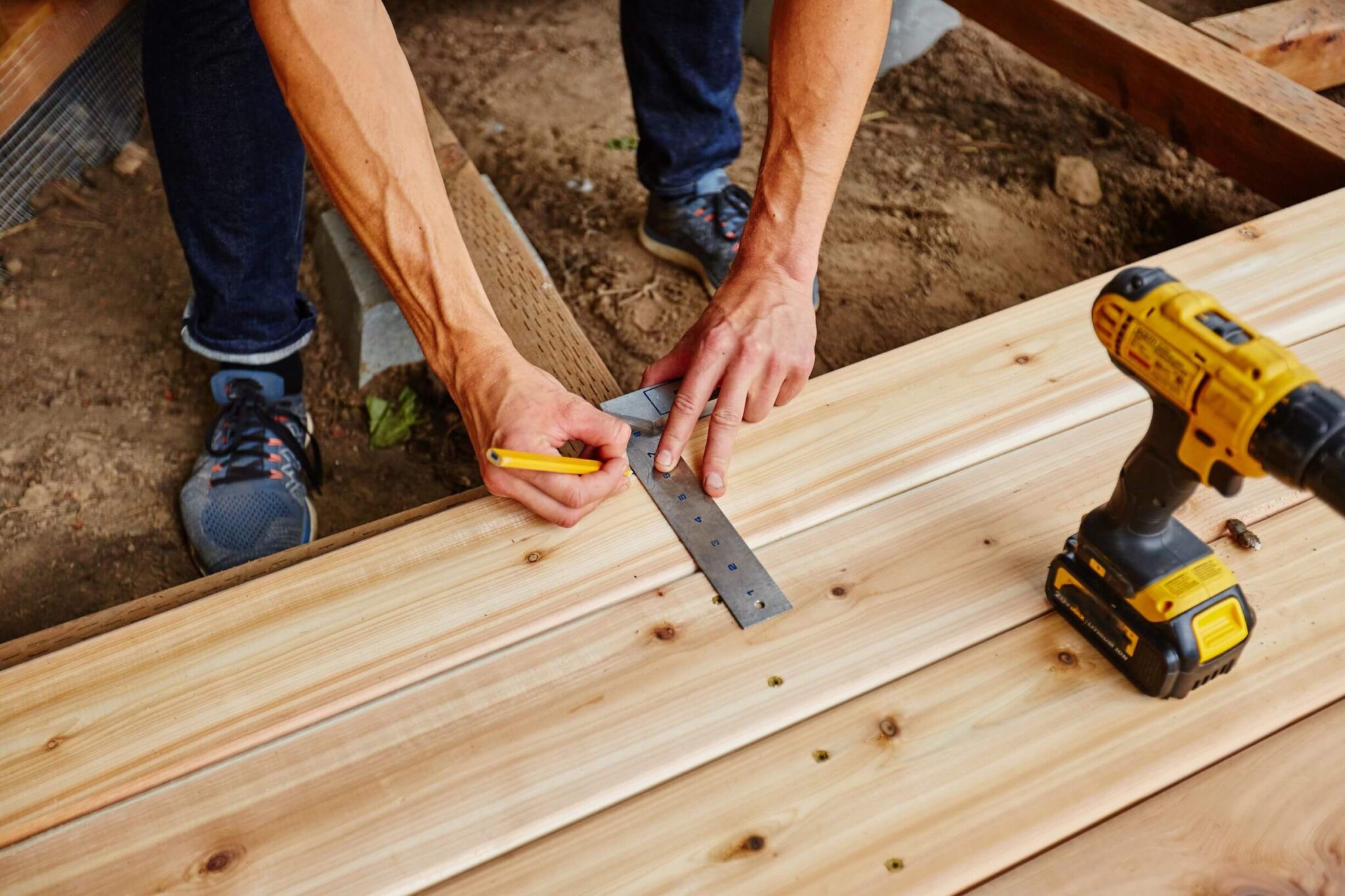 un paysagiste mesure la largeur du lame de terrasse ne bois